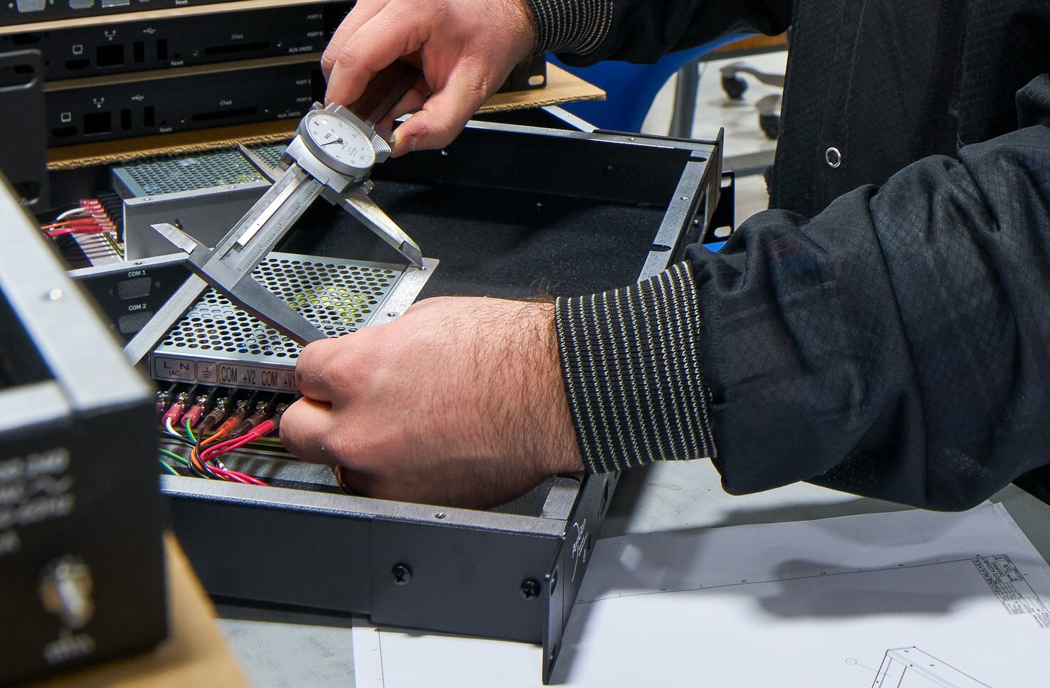 Up close on computer technician's hands holding a caliper on a computer component to determine form fit.