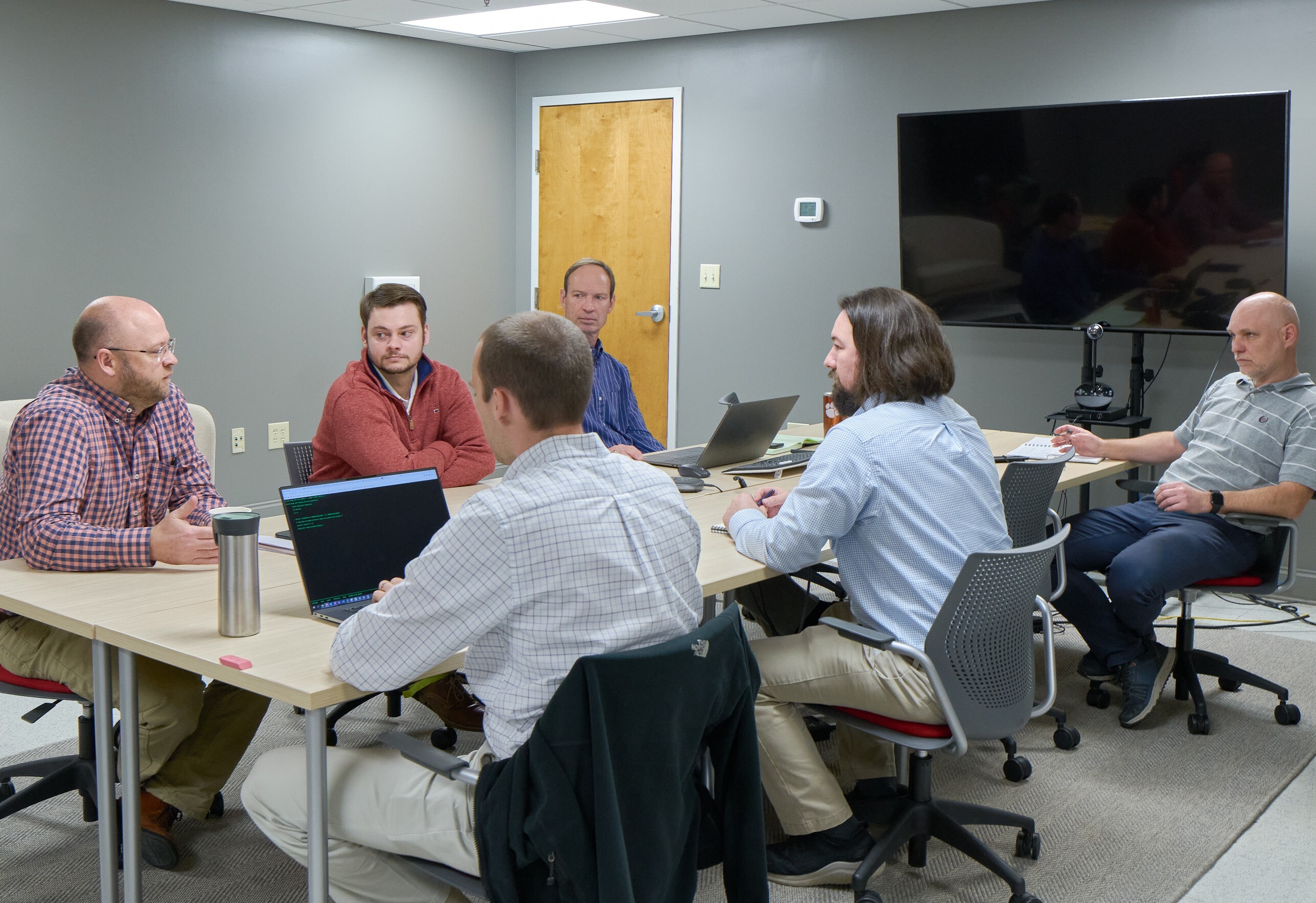 Several engineers sitting a table with computers on the table.