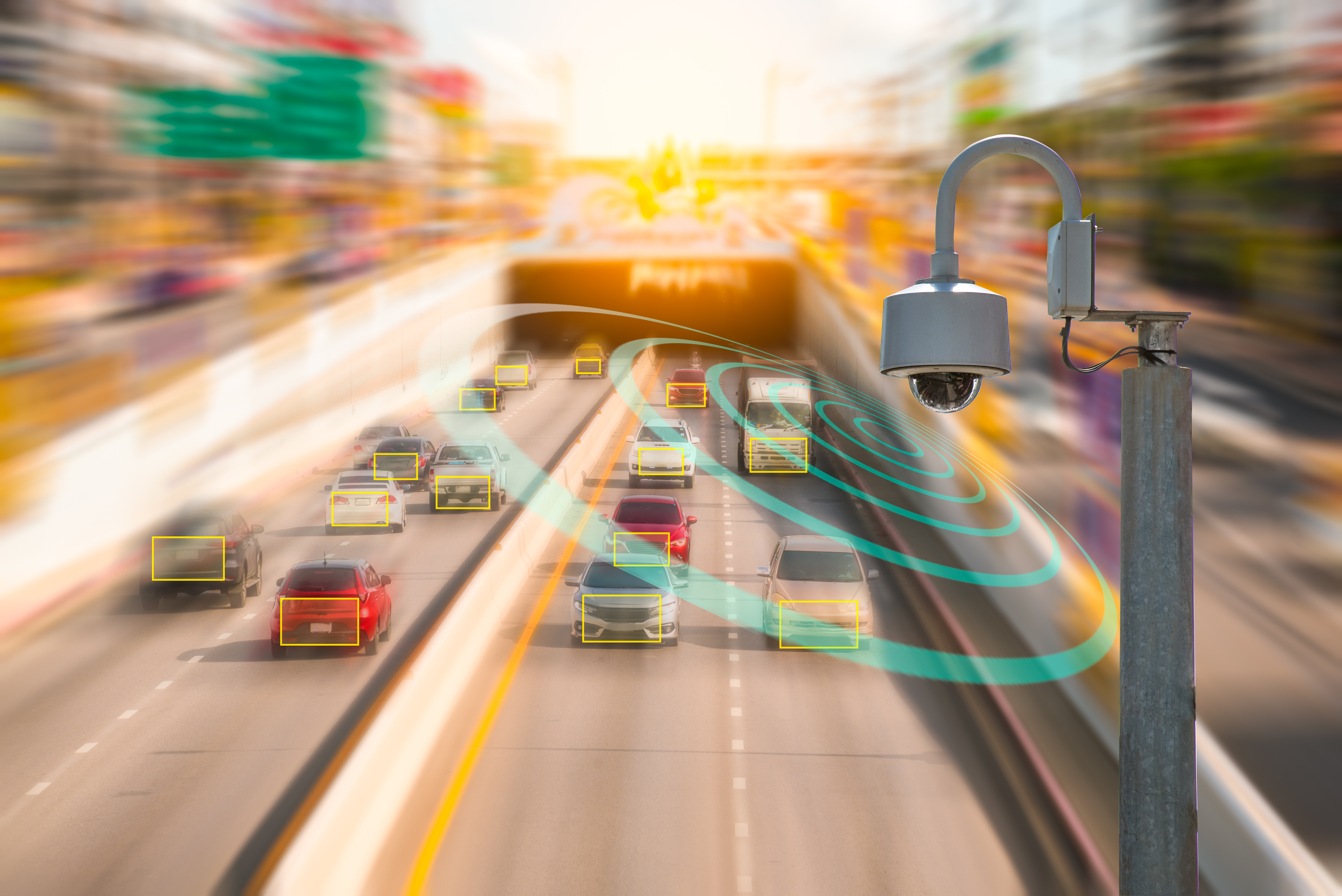 Traffic camera attached to a pole over a highway with traffic on both sides.