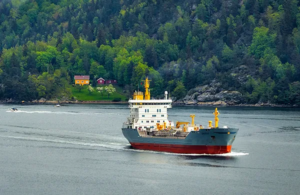 A marine cargo ship piloting close to a forested shoreline